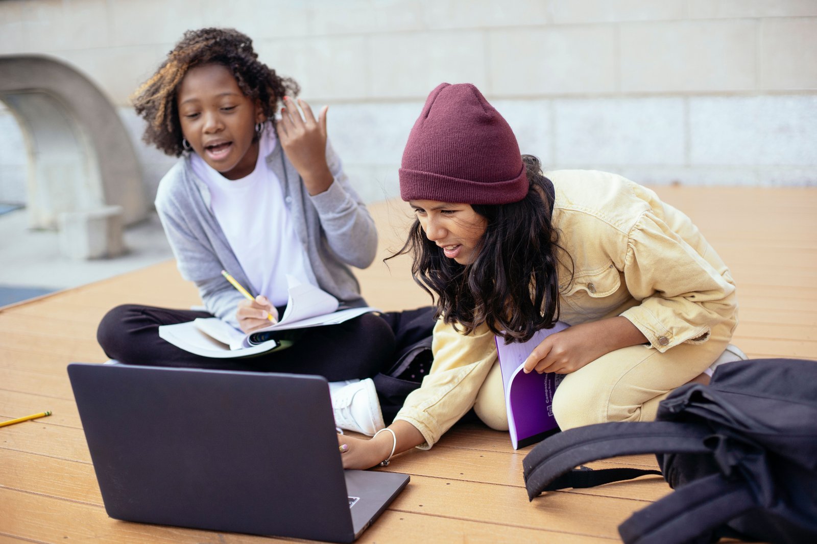 two girls working together on a laptop outside